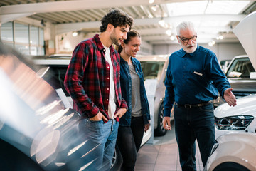 Car dealer showing car to couple in showroom