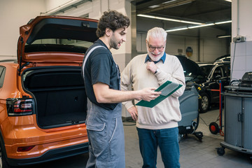 Car mechanic explaining check list to client in workshop