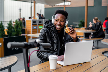 Man using laptop and eating a burger in a cafe