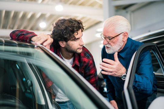 Car dealer showing car to young man in showroom