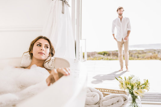 Young woman relaxing in bathtub with man in background