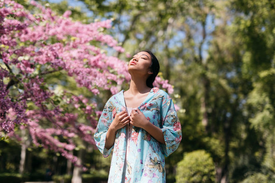 Beautiful young woman with blooming cherry tree in a public garden in spring