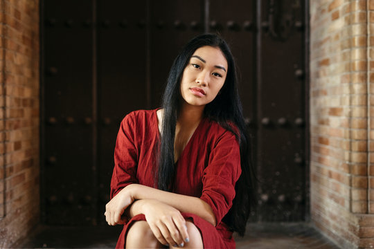 Portait of beautiful young woman wearing a red dress sitting in front of a door