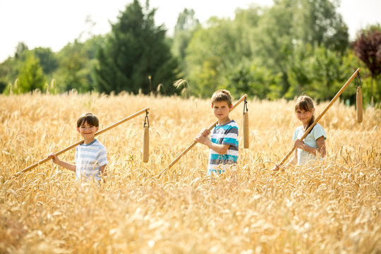 Children learning how to flail wheat in field