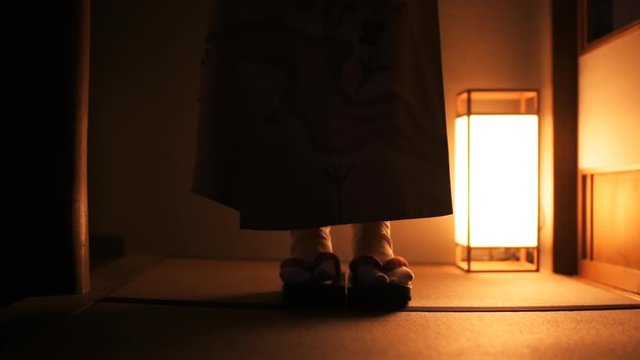 Slow motion of traditional Japanese house ryokan with tatami mat floor, shoji sliding paper doors and woman in kimono and geta shoes tabi socks front walking in corridor hall room