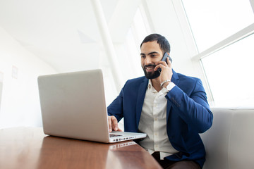 successful businessman in a suit uses a laptop and talking on the phone in a white office at the workplace