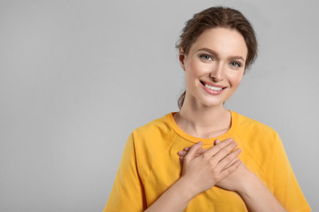 Beautiful grateful woman with hands on chest against light grey background. Space for text - obrazy, fototapety, plakaty
