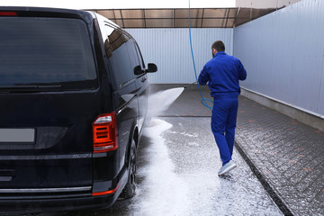 Worker cleaning automobile with high pressure water jet at car wash