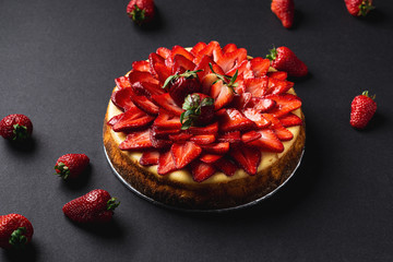 Strawberry Cheesecake on dark background. A classic decadent dessert, this sweet and delicious homemade baked cheesecake is topped with fresh strawberry slices. The perfect cake for a birthday.