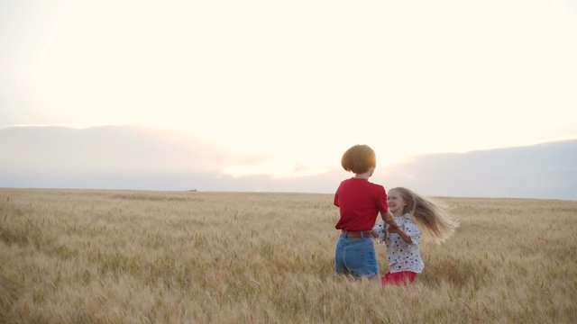two smiling children sisters enjoying at the wheat field at the bright summer evening