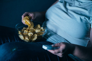 Emotional eating, mental disorder, depression, loneliness, stress. Fat overweight woman lay on the coach with tv remote and junk food.