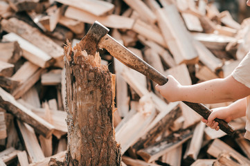 Picture of beautiful chubby girl stands with an axe against the background of a large pile of firewood