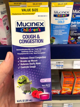 Alameda, CA - Nov 24, 2019: Hand holding box with children's medication in front of store shelf showing label. Mucinex, cough and congestion treatment. Berry flavor.