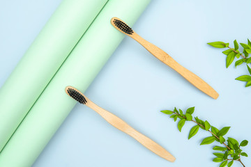 Bamboo wooden toothbrushes with green leaves on blue pastel background. Dental health medical care concept. Copy space. Eco friendly goods, environment care protection