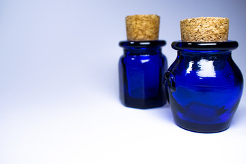 Two blue bottles with corks, oval and hexagonal bottle, white background some shadows, one focused...
