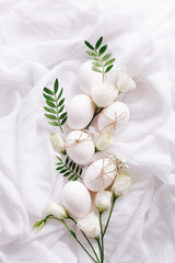 White Easter eggs with flowers and green leaves on white fabric background