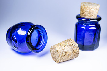Two blue bottles with corks, oval and hexagonal bottle, white background some shadows, one focused...