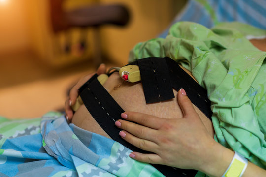 Mid adult pregnant woman with ctg monitor on belly