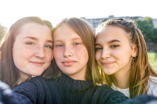 Three teenage girls of 12-14 years old, summer city watching videos phone, happy smiling people having fun rejoice. Selfie portrait close-up. Casual clothes, sweaters. Emotions of positive relaxation.