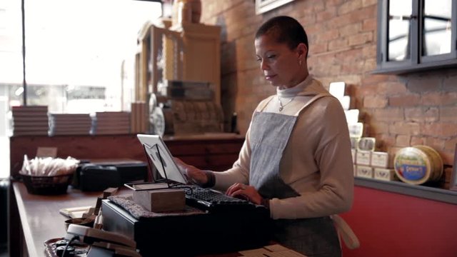Female shop owner using digital tablet cash register at counter
