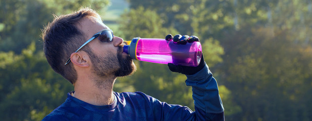 Cyclist drinking water from a purple sports bottle on green hills