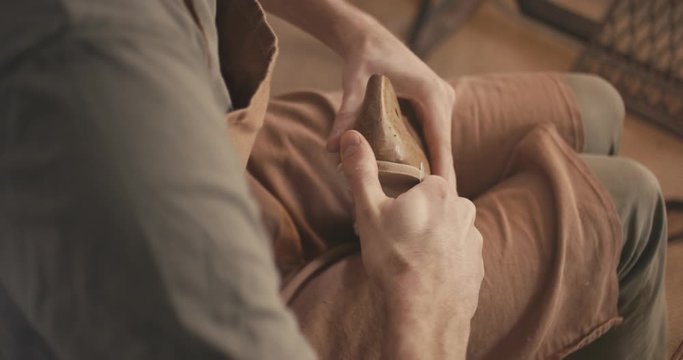 Traditional bespoke shoemaker cutting shaping leather insole on wooden shoe last with knife over the shoulder