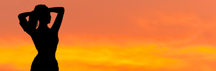 A young slim athletic girl in sportswear performs a set of exercises. Fitness and healthy lifestyle..Silhouette at sunset.