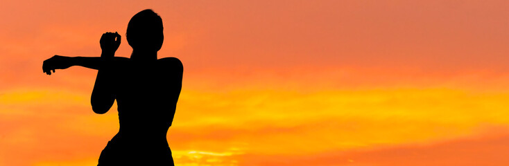 A young slim athletic girl in sportswear performs a set of exercises. Fitness and healthy lifestyle..Silhouette at sunset.