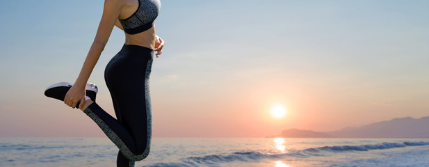 Fototapeta premium A thin athletic girl takes a break between classes on the background of the sunset by the sea in the early morning, enjoys silence and freedom.