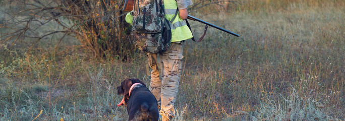 A man with a gun in his hands and an green vest  on a pheasant hunt in a wooded area in cloudy...