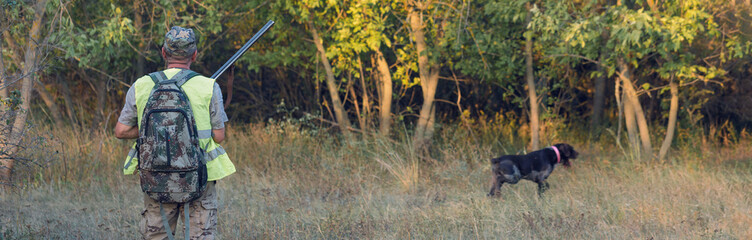 A man with a gun in his hands and an green vest  on a pheasant hunt in a wooded area in cloudy...