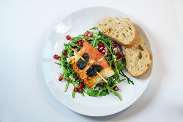 Fried chicken saltimbocca wrapped with prosciutto ham and sage leaves served on arugula salad and with bread on a plate on a white table, copy space, high angle view from above