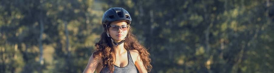 Girl on a mountain bike on offroad, beautiful portrait of a cyclist at sunset, Fitness girl rides a modern carbon fiber mountain bike in sportswear. Close-up portrait of a girl in a helmet and glasses