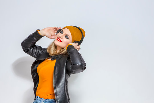 Portrait of Relaxing Caucasian Female Listening to Music Wearing Headphones. Posing in Leather Jackaet and Warm hat on White