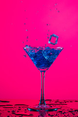 Splashes and Droplets of Drink Spilling Out of The High Glass Goblet with Ice Cubes and Colorful...