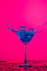 Droplets of Alcohol Drink Spilling Out of The High Glass Goblet with Ice Cubes and Colorful Liquid. Isolated Over Colorful Background.