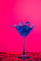 Drink Spilling Out of The Glass Goblet with Icecubes and Colorful Liquid. Isolated Over Colorful Background.
