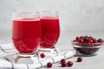 Two glasses with homemade freshly cranberry juice and a bowl of cranberries on a gray concrete table