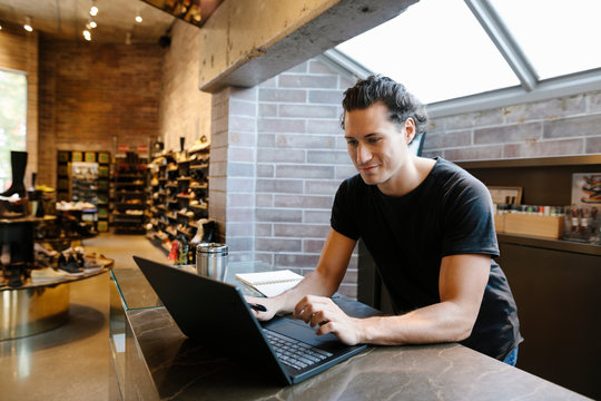 Boutique shoe store owner using laptop and smiling