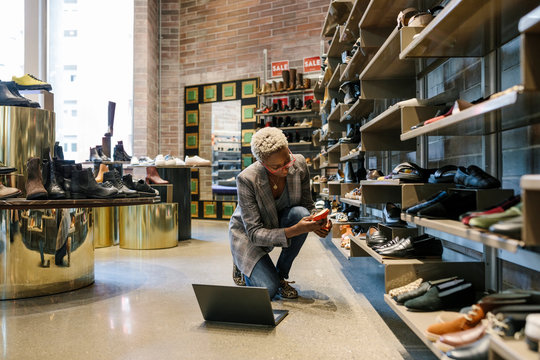 Mid adult woman working in shoe store with laptop