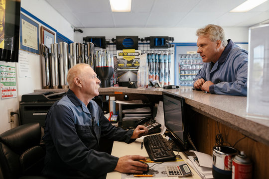 Mechanic using computer and talking to colleague in auto parts shop