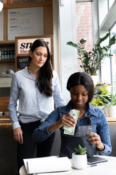 Female cafe owner supervising employee cashing up