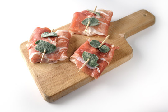 Prepared chicken saltimbocca wrapped with air-dried ham and sage leaves on a kitchen board isolated on a white background, copy space, selected focus