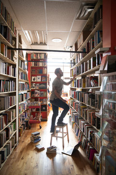 Mid adult man standing on stool in book store