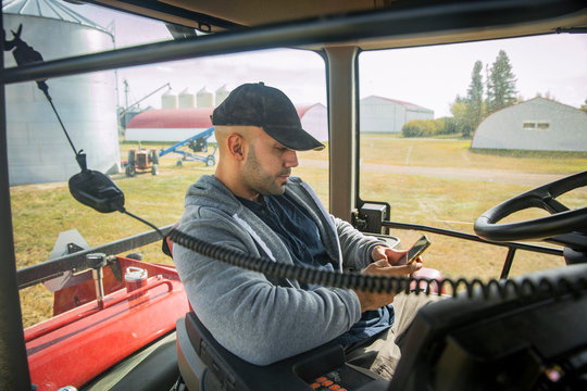 Male farmer using smart phone inside tractor