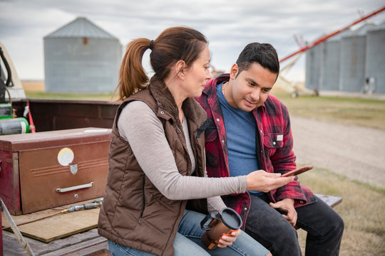 Farmers Drinking Coffee And Using Smart Phone At Truck Bed On Farm