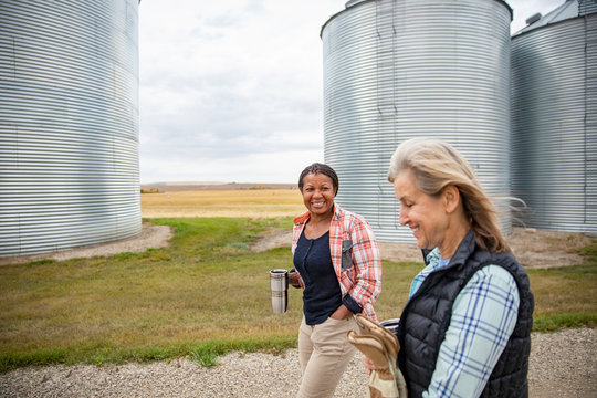 Female farmers drinking coffee and walking along silos on farm