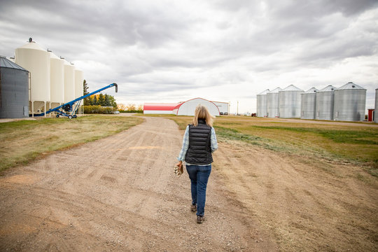 Senior Female Farmer Walking Toward Silos In Farmyard