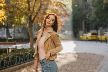 Beautiful white woman in beige jacket spending leisure time in park. Outdoor portrait of romantic ginger lady standing on alley in sunny day.