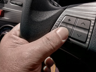 hand on steering wheel, finger touching the volume button on the steering wheel